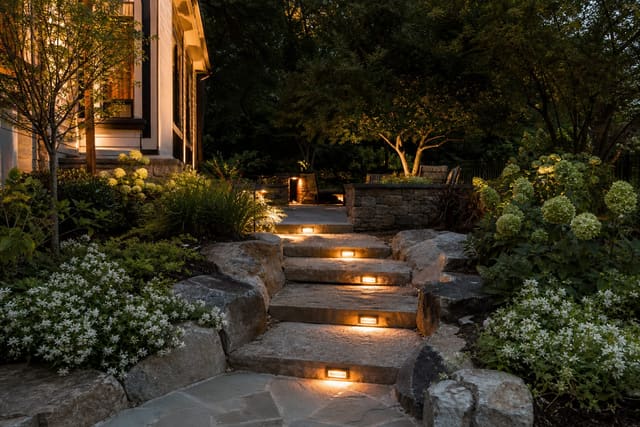 warm low-glare lights tucked into stone garden steps with planting beds and a softly lit path at dusk