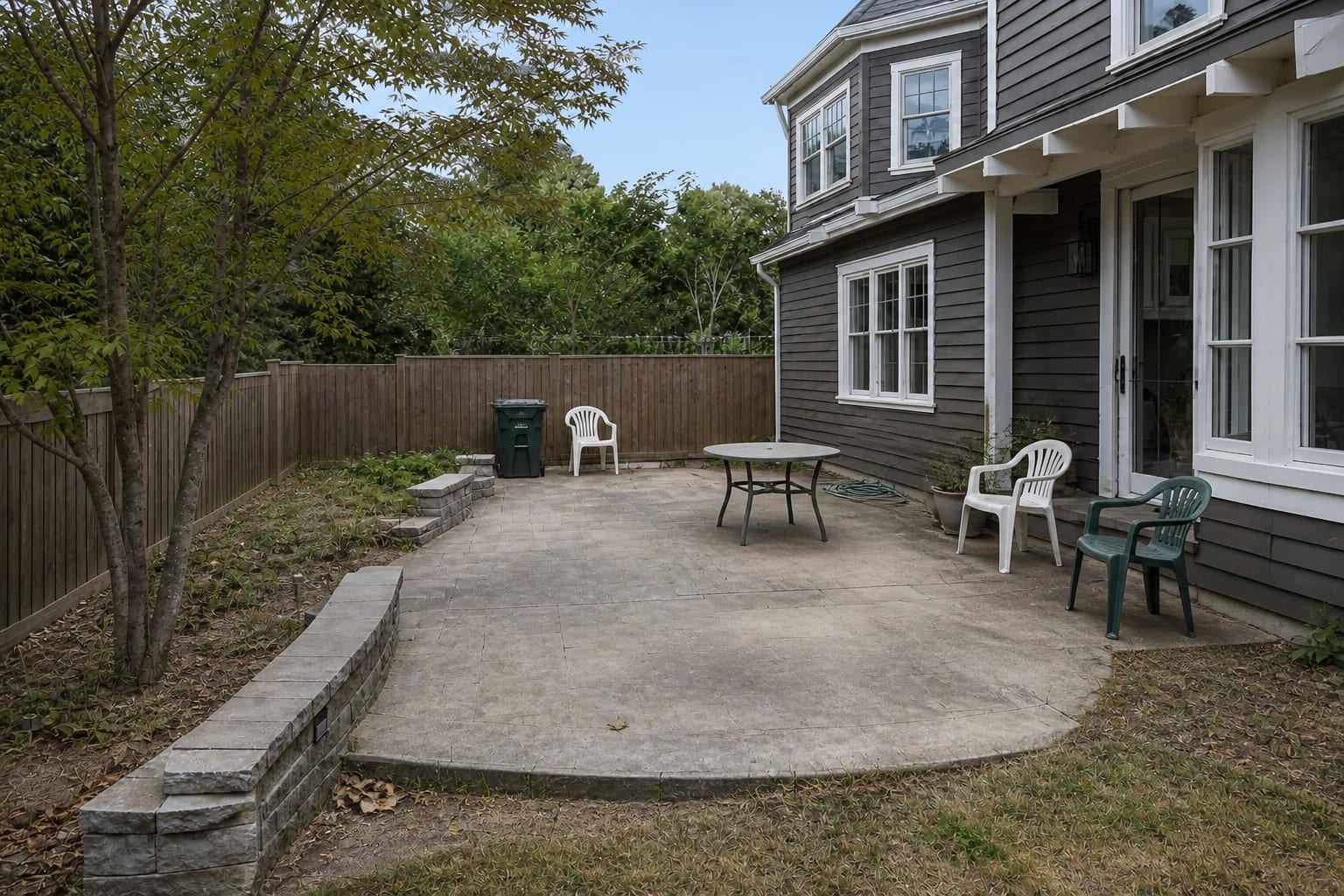 small outdoor patio with plain stone-like slab, mismatched chairs, bare edges, and no clear dining shape