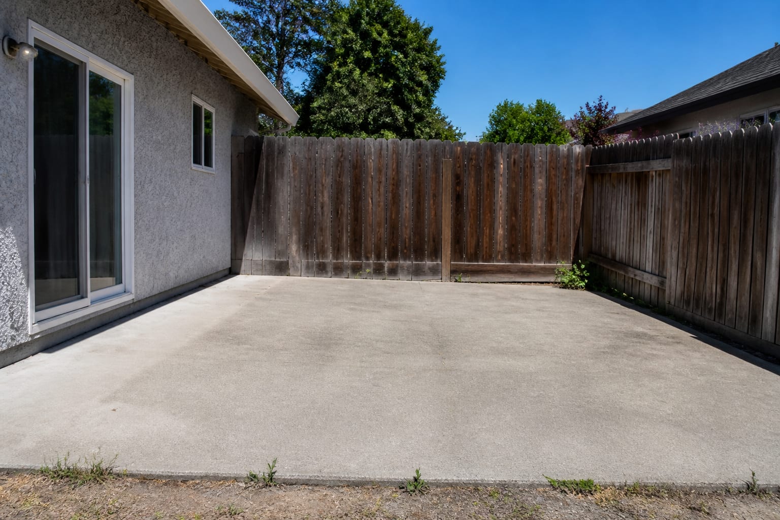 A bare concrete backyard patio with no furniture or shade