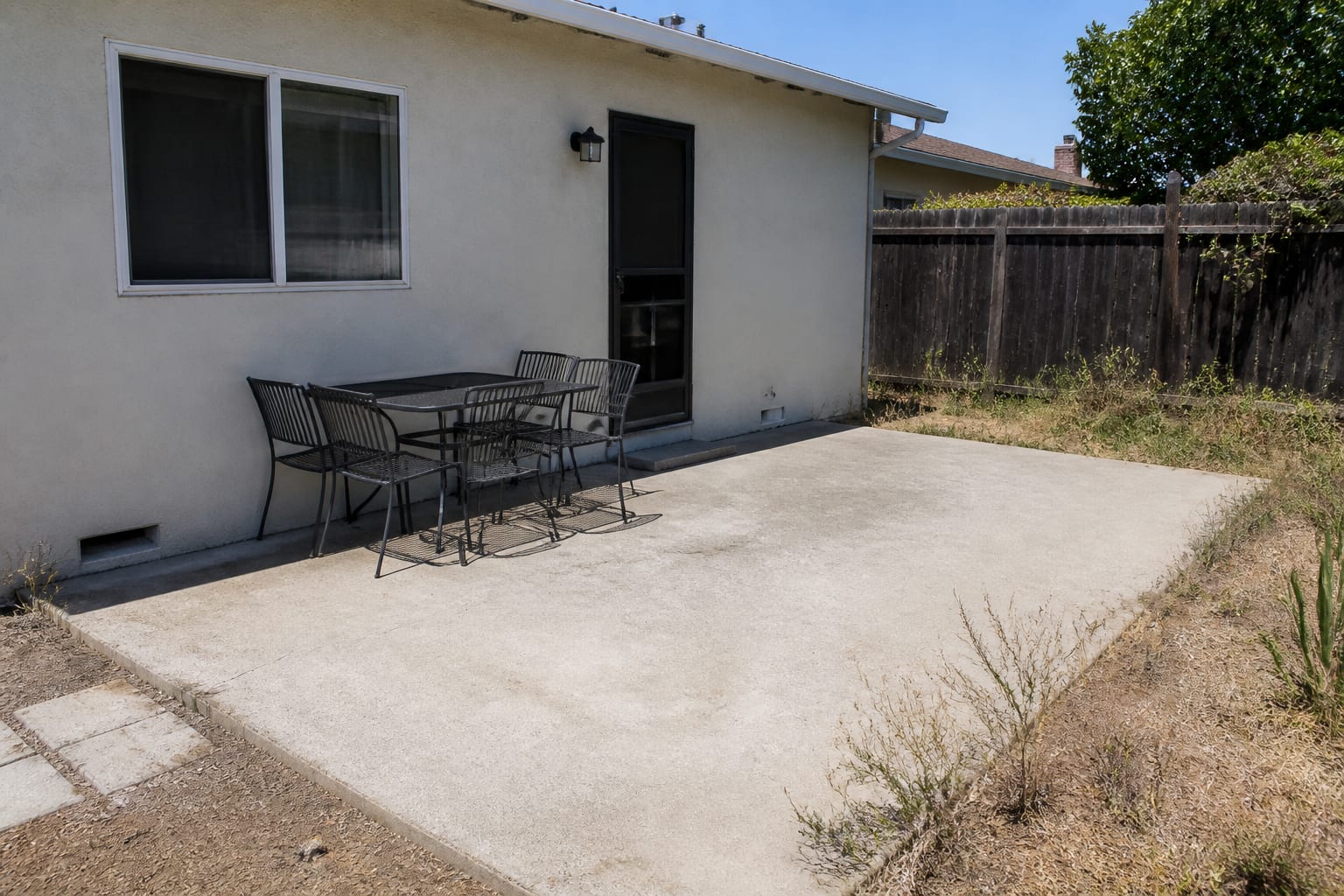 Bare concrete patio with a plain table and chairs and no shade or greenery