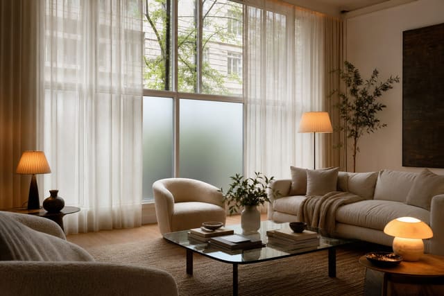 layered sheers and lower frosted glass on a living room wall of windows with warm lamps and pale upholstery