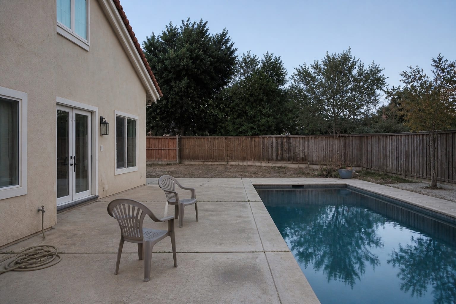 under designed concrete pool patio with plastic chairs, harsh exposed fence, and no planting or shade structure