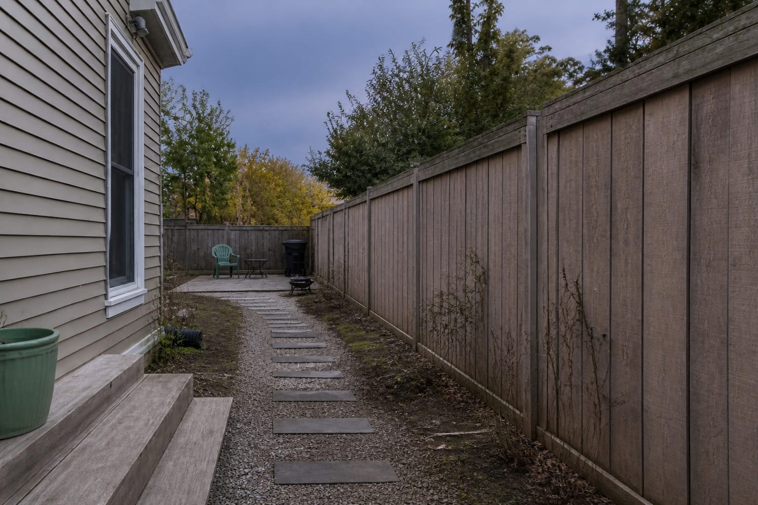 flat garden path beside a plain fence with no vertical structure, sparse planting, and an exposed view into the yard
