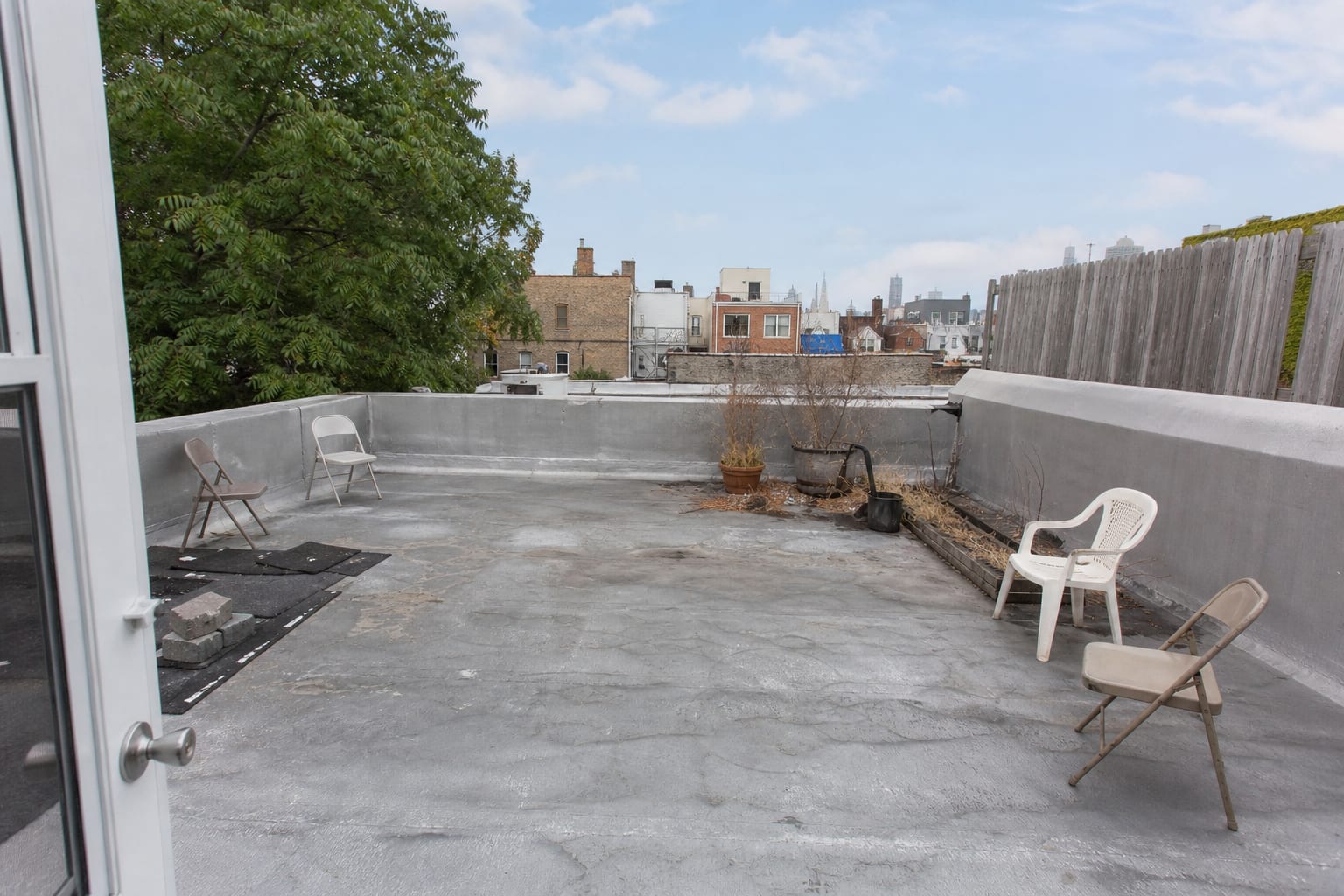 unfinished urban rooftop with plain membrane surface, scattered folding chairs, exposed mechanical edges, and no shade or seating plan