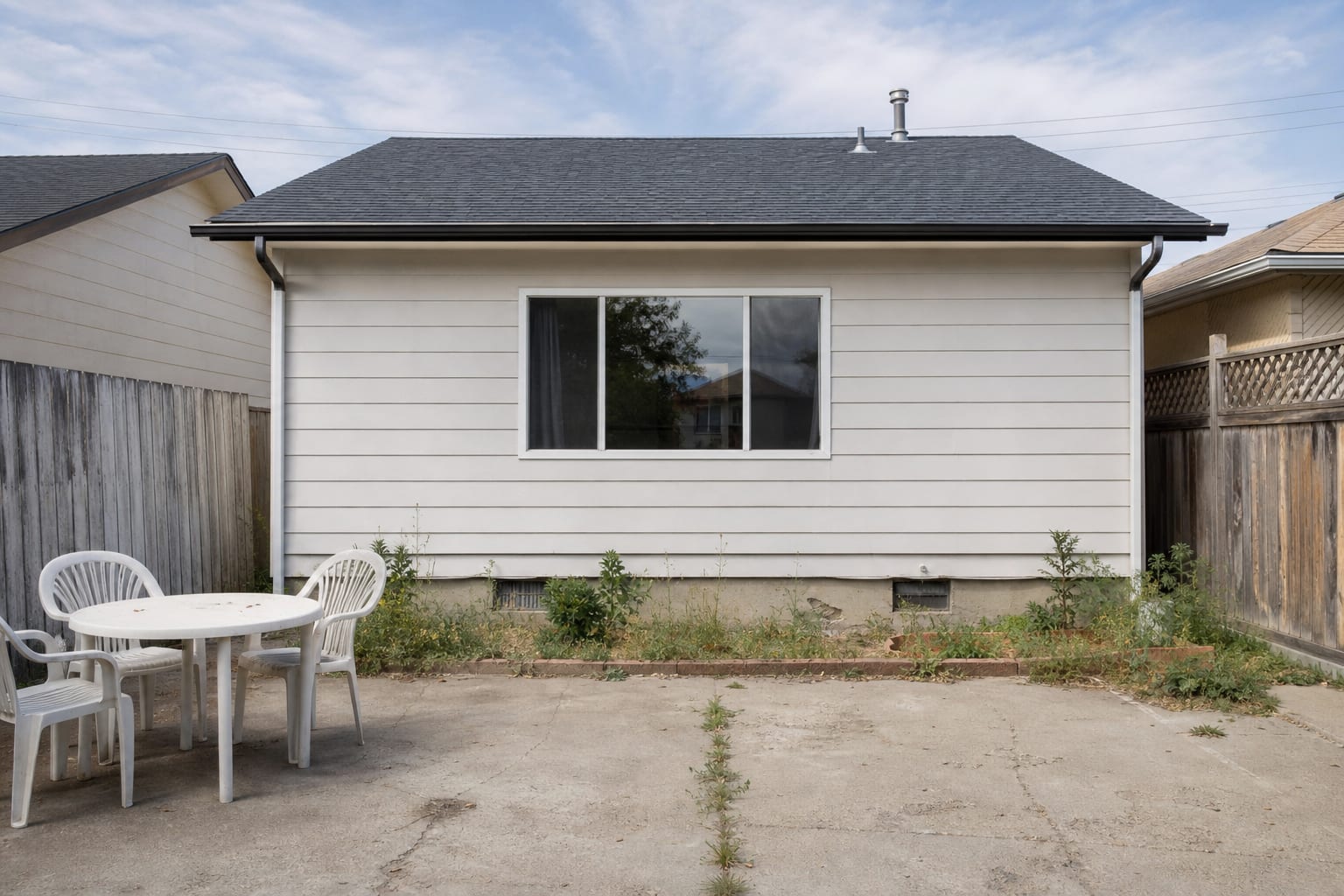 flat front facade with a bare window, plain siding, narrow sill, and no planting to soften the exterior wall.