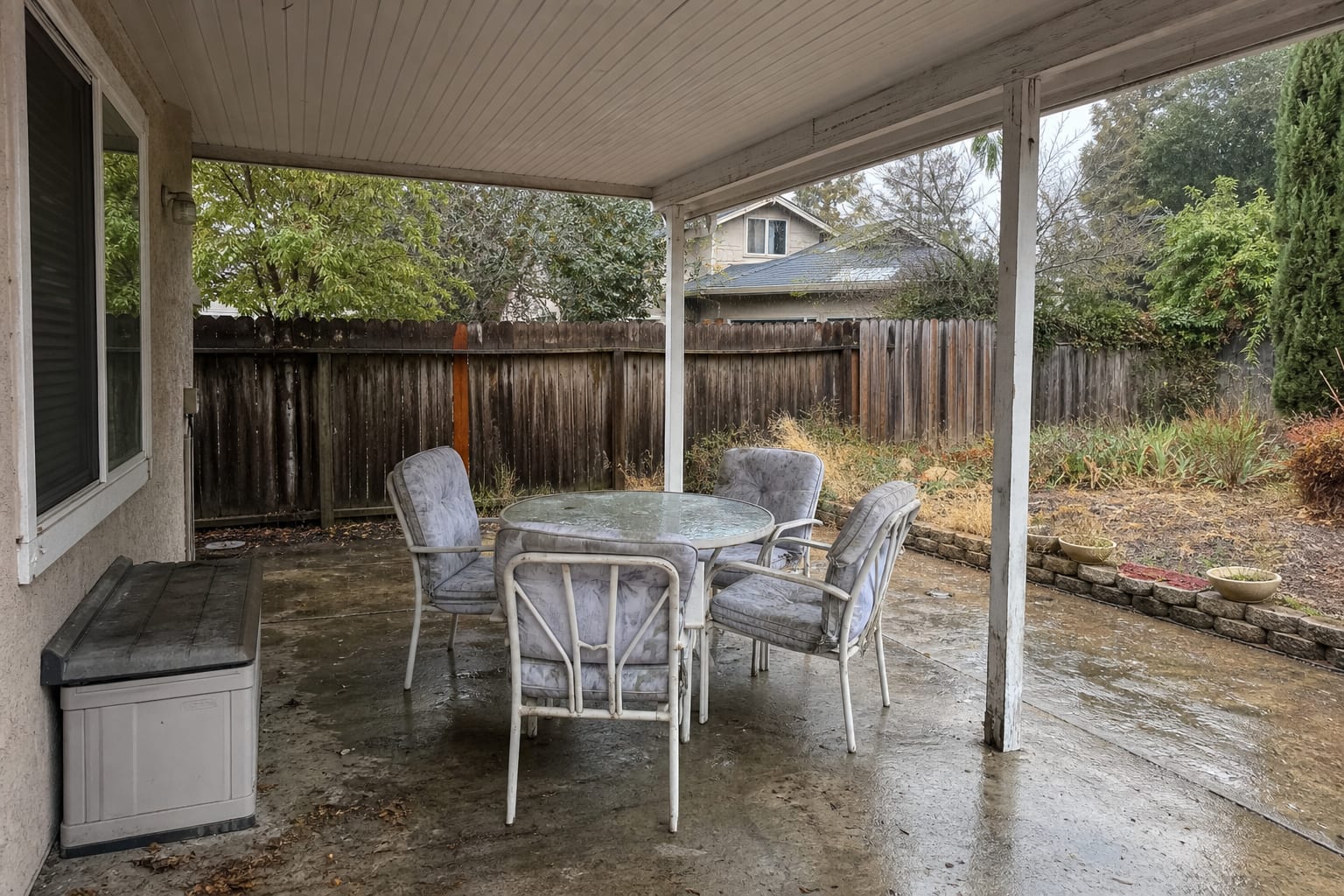 under designed patio after fall use with damp cushions left on chairs, uncovered table legs on wet paving, and no clear winter storage zone.